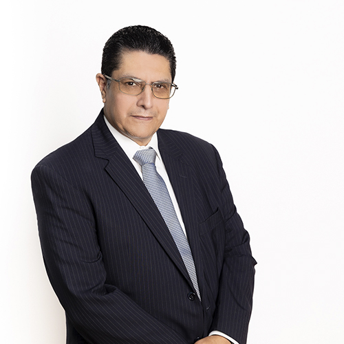 Un hombre de mediana edad con gafas y un traje azul marino posa con confianza, representando el liderazgo de nuestra clínica dental.