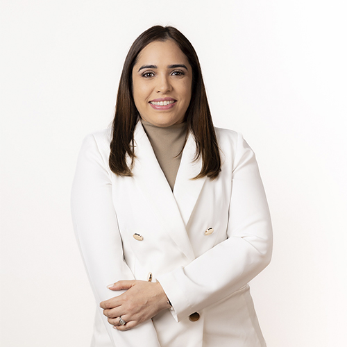 Una dentista experimentada con una cálida sonrisa y una bata blanca de doble botonadura, posa en nuestra clínica dental profesional.