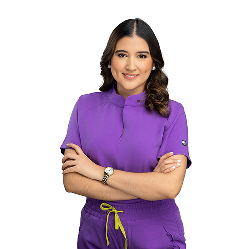 Dra. Scarlett Estrada posa de brazos cruzados con uniforme médico profesional para el sitio de la clínica dental.