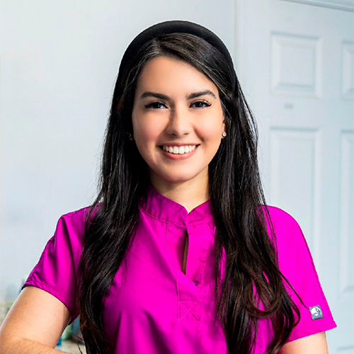 Dra. Delmy Lainez sonríe con uniforme fucsia, preparada para atender a los pacientes dentro de la clínica dental.