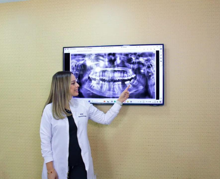Una odontóloga sonriente apuntando a una radiografía dental panorámica mostrada en una pantalla grande en la consulta dental.